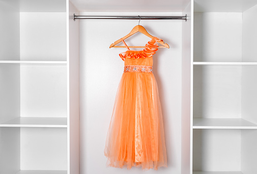 Big white modern wardrobe with empty shelves and orange vintage dress hanging on wooden rack.