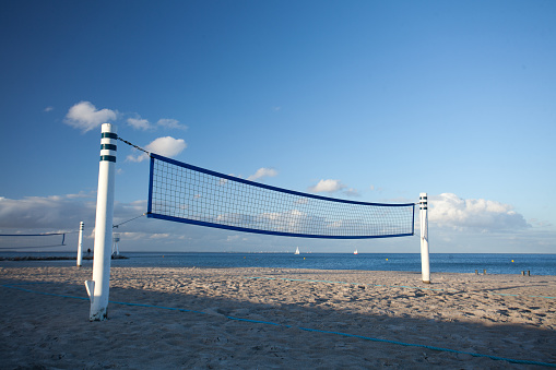 A multi-colored beach volleyball in mid-air after hitting just pass the red baseline tape on a sand court.