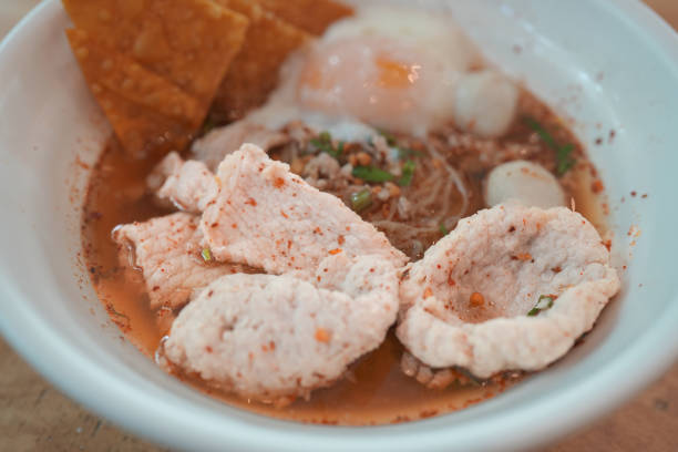 Thai local spicy noodle Tom Yum soup with marinated pork and half boiled egg in white bowl.