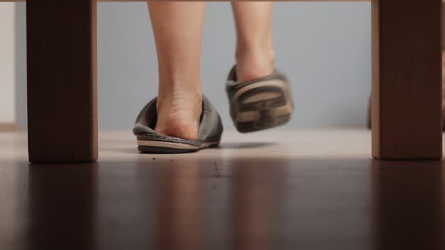 Unrecognizable barefoot woman getting out of bed and wearing warm slippers on floor in bedroom in morning after waking up