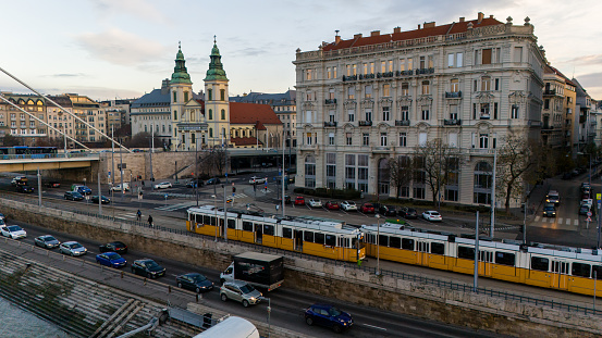 Hovering Above,a Drone Captures the Dynamic City Life of Budapest,Hungary,with Trams Gliding on Roads Beside Historic Buildings and The Parish Church. This Aerial View Encapsulates the Fusion of Modernity and History,Creating A Captivating Snapshot of Urban Vitality
