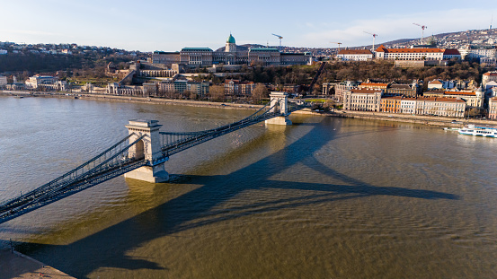 Captured from a Lofty Perspective,an Aerial Drone Reveals the Sun Kissed Elegance of the Szechenyi Chain Bridge Gracing the Danube River Amidst the Charming Cityscape of Budapest,Hungary. The Scene Radiates with the Warmth of a Sunny Day