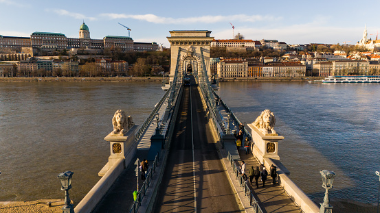 From a High Angle Drone Perspective,the Szechenyi Chain Bridge Over the Danube River in Budapest,Hungary Comes Alive During a Sunny Day. The Bridge Buzzes with Life as People Traverse its Iconic Structure