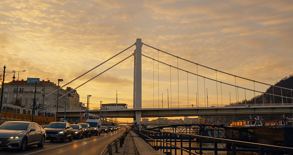 A Low Angle View Captures the Tall Elisabeth Bridge Over a Busy Road Against the Vibrant Sky During Sunset in Budapest,Hungary. The Scene Radiates a Sense of Dynamic Urban Energy Against the Backdrop of the Evening Sky
