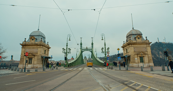 City Transit in Motion,a Tram Gracefully Moves Across Liberty Bridge Against the Budapest Sky in Hungary. The Scene Captures the Dynamic Energy of Urban Transportation Against the Iconic Cityscape