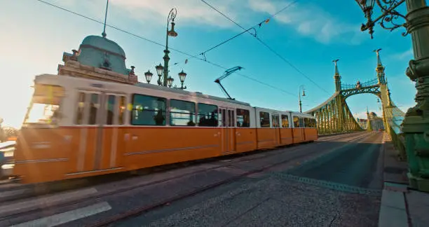 Sunny Day Commute,Blurred Motion Captures the Tram Gracefully Moving on Liberty Bridge Against the Blue Sky During a Sunny Day in Budapest,Hungary. The Scene Radiates the City's Dynamic Charm and the Joy of Urban Transit