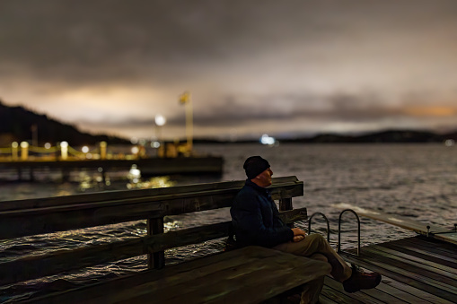 Stockholm, Sweden A man sits on a bench on a small dock in Lake Malaren at night in the Ekero suburb.