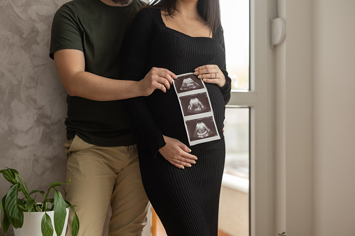 Future parents with ultrasound picture of their future child, in living room at home.