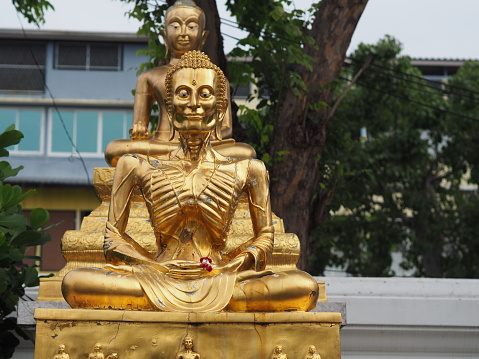 Yellow-gold Buddha statues, green-gray leaves and black-and-white buildings, indigo silver, white clouds are used as backgrounds.