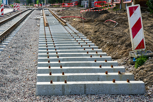 New tram rail track construction site with concrete sleepers on rubble base, warning signs and plastic warning barriers