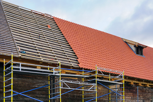 Installation of new red clay tiles on new wooden battens on the roof of a historic house, installing clay roof tiles