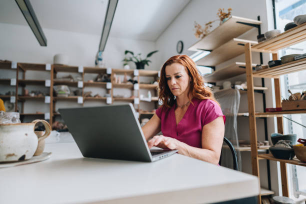 istock Mature woman working on laptop at her ceramic store 1884487792