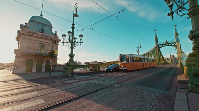 Handheld Shot of Tram and Car Passing on Liberty Bridge During Sunny Day Against Blue Sky at Budapest,Hungary