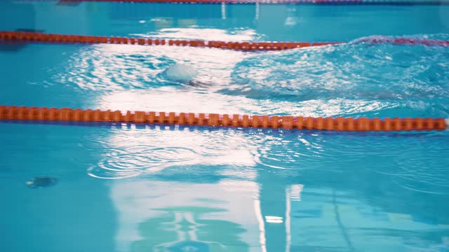 A professional man athlete trains in the pool. A male swimmer swims the butterfly stroke in his swim lane and finishes.