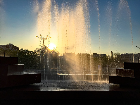 Fountain in the city park on a background of the setting sun