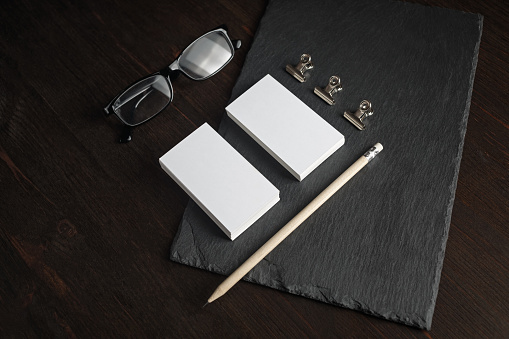 Photo of blank stationery set. Blank business cards, pencil, glasses and clips on stone board.