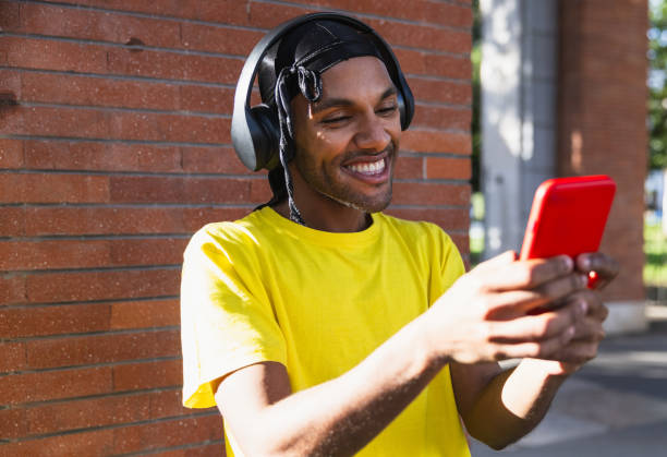 istock Young black guy with helmets smiling while acting with cell phone on the street 1884639055