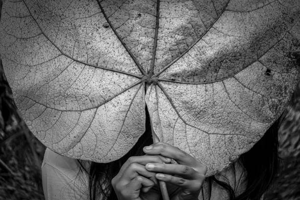 girl's hands cover her face with leaves