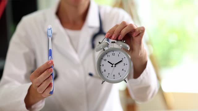Doctor dentist showing alarm clock and toothbrush in clinic closeup 4k movie slow motion