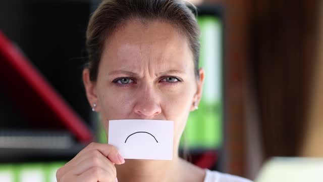 Tired woman bringing to her face piece of paper with drawn sad smile 4k movie slow motion