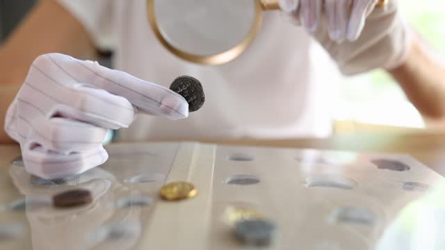 Numismatist in white gloves looking at ancient coins with magnifying glass closeup 4k movie slow motion