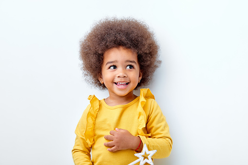 cheerful fluffy african american girl looking happy holding magic wand in hands, laughing, isolated on white studio background. portrait. people diversity, african ethnicity, childhood concept