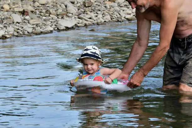 Laughing little girl learns to swim in a river in nature with a rescue inflatable wheel