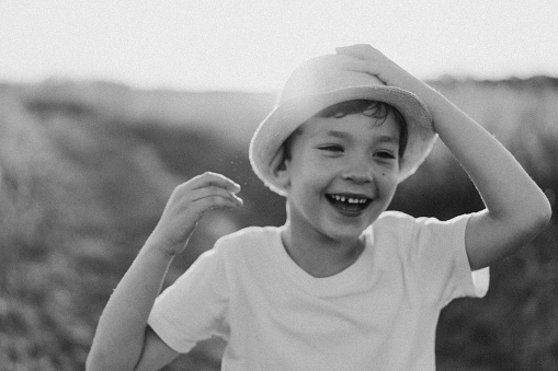 Portrait of a smiling little boy in a white T-shirt and hat playing outdoors on the field at sunset. Happy child, lifestyle. Products for children.