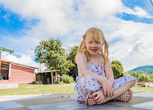 portrait of albino girl sitting outdoors while wearing a dress and two tails in her hair while smiling