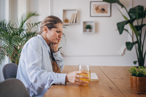 A middle-aged woman suffers from tooth pain while drinking a cold beverage at home, grimacing in discomfort