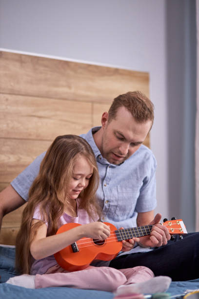 istock father teaching guitar and ukulele to his daughter, learning 1884850235