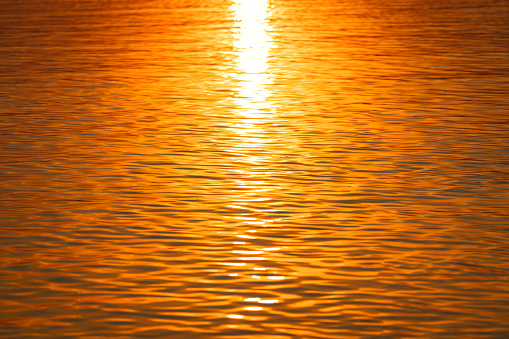 Water surface with reflection of orange sunlight during sunset time. Abstract background and texture scene.
