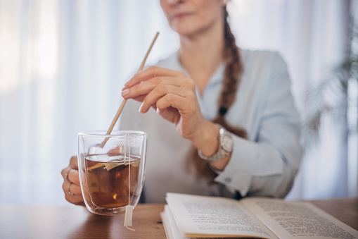 A joyful middle-aged Caucasian woman sips her tea through a straw, smiling as she avoids tooth sensitivity, in a bright and airy room.