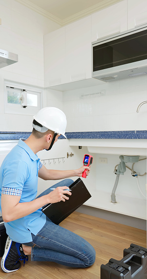 asian male home inspector is using thermal imager to check water leakage situation at kitchen sink tube