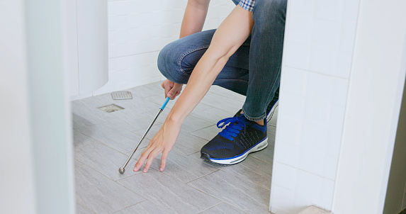 close up asian male home inspector is using telescopic hollowing drum detection hammer to check bathroom interior