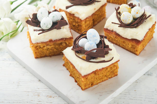 istock Easter carrot cake bars decorated with chocolate nest and chocolate candy eggs blossoming cherry or apple flowers on rustic light wooden backgrounds. Easter holiday meal. Traditional Easter food. 1884891825