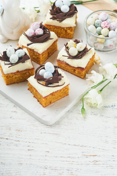 istock Easter carrot cake bars decorated with chocolate nest and chocolate candy eggs blossoming cherry or apple flowers on rustic light wooden backgrounds. Easter holiday meal. Traditional Easter food. 1884892173