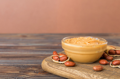 Bowl of peanut butter and peanuts on table background. top view with copy space. Creamy peanut pasta in small bowl.