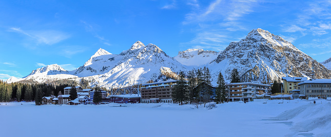 Panorama view of the popular resort Arosa in Canton Grison with the frozen Obersee lake and the snow-covered Alps peaks Weissfluh, Tierjer Flue and Amselflue.