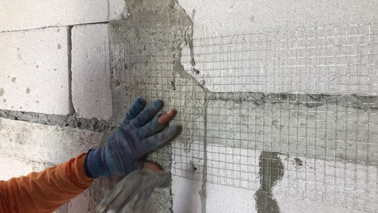 Construction workers are hammering nails into the steel grid before plastering the lightweight brick wall.