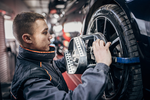 Male mechanic sets the wheel alignment equipment on a car wheel in auto repair shop.