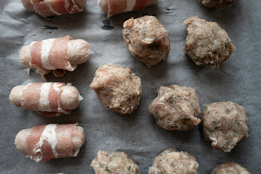 Freshly made meat balls seen with bacon wrapped sausages on a backing tray seen before being placed in a oven.