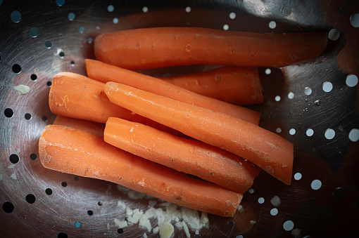 Close-up of fresh carrots seen soon after being boiled and placed in a metal colander being drained and served for a roast dinner.