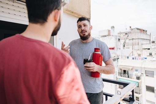 Mid adult man talking with friend in the balcony at apartment