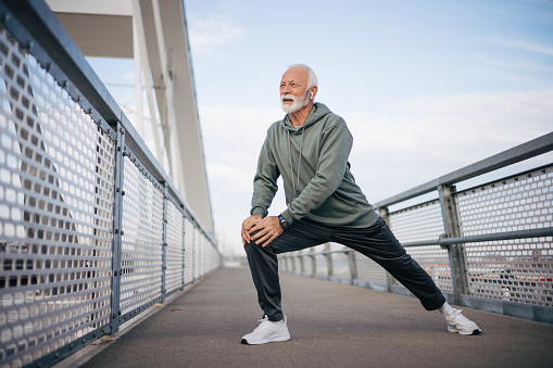 A mature man stretches his legs on the bridge and warms up for training