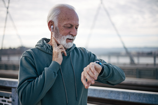 Senior man measuring heart rate pulse on his neck and looking on watch