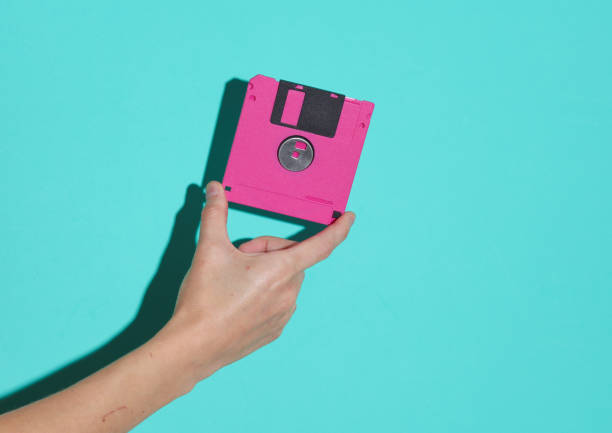 istock Hand holding pink retro 80s floppy disk on a blue background 1884960846