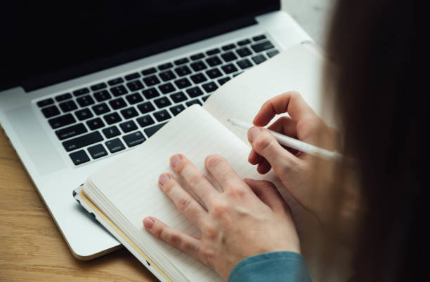 istock A woman takes notes in a notepad using a laptop sitting at the table. 1884962084