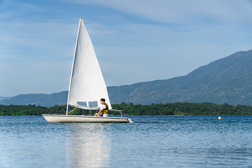 Young person sailing a small sailboat on the lake on a beautiful summer day.