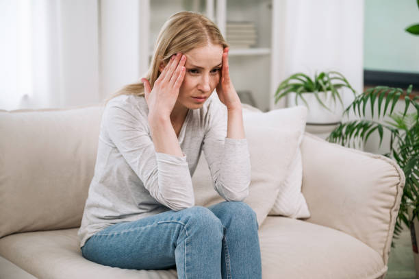 istock stressed woman feeling bad, hold head and sitting on couch 1884988428